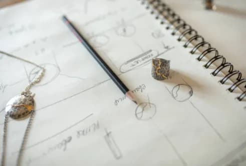 Jewellery design sketchbook with pencil drawings, loose gemstones and a design pencil on open pages