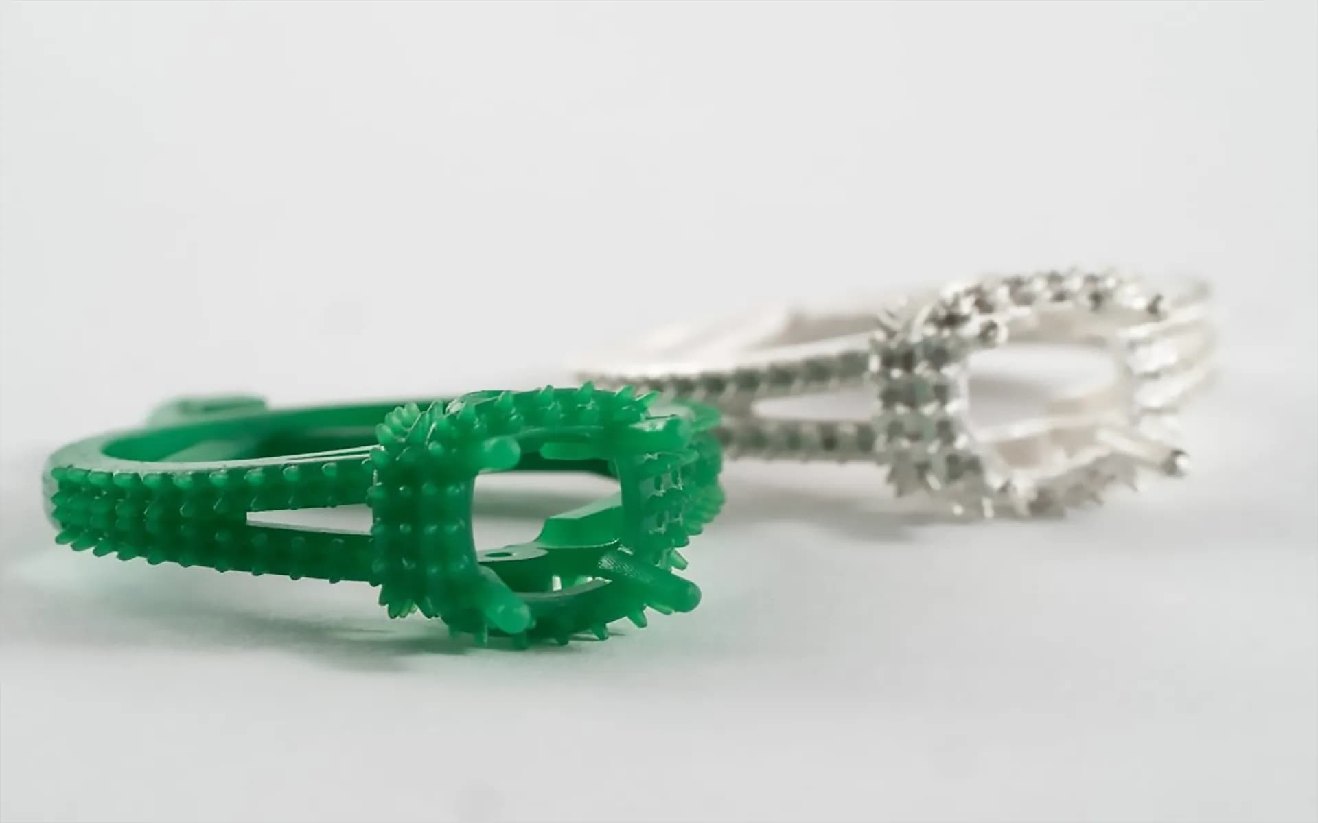 Green 3D-printed wax ring model beside a finished white gold cast ring set with diamond-like stones