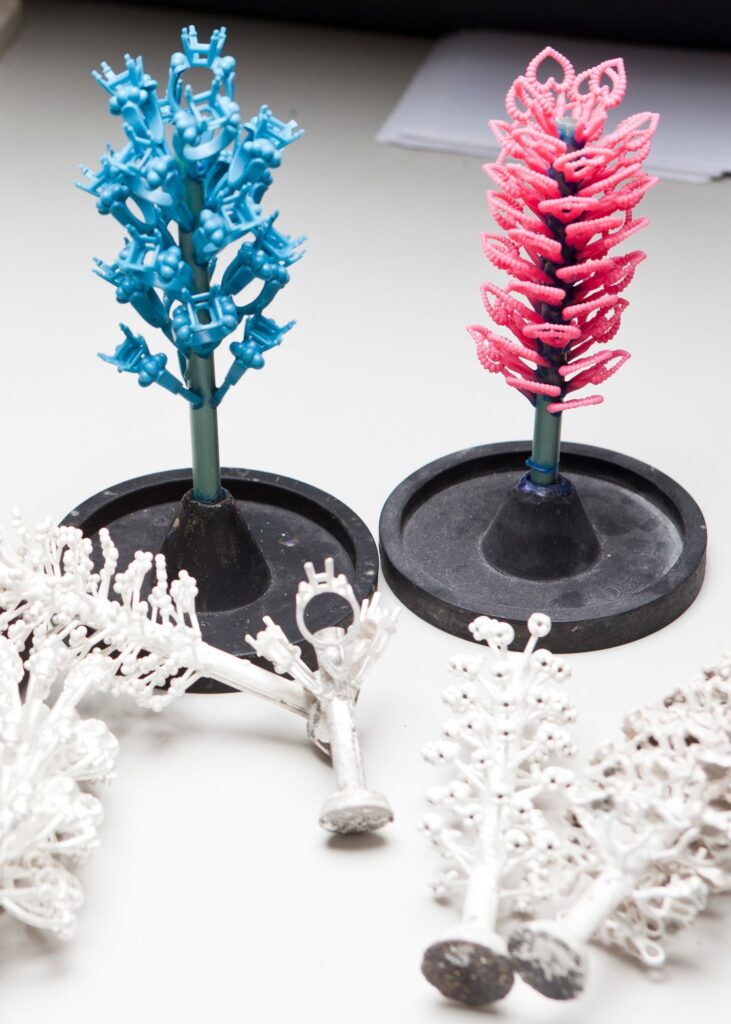Blue and pink 3D printed jewelry casting tree with white gold cast rings and sprue system on black investment flasks