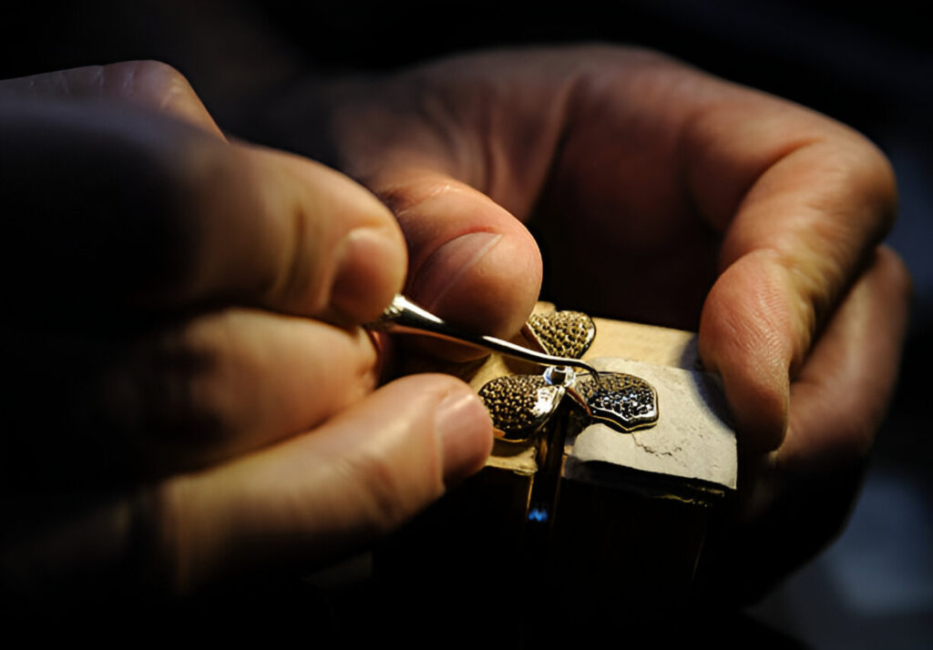 Jewelry artisan burnishing gold pendant with textured surface using precision hand tool in workshop lighting