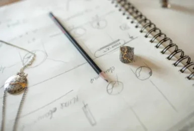Sketching Jewelry design sketchbook with pencil drawings, loose gemstones, and design pencil on open pages